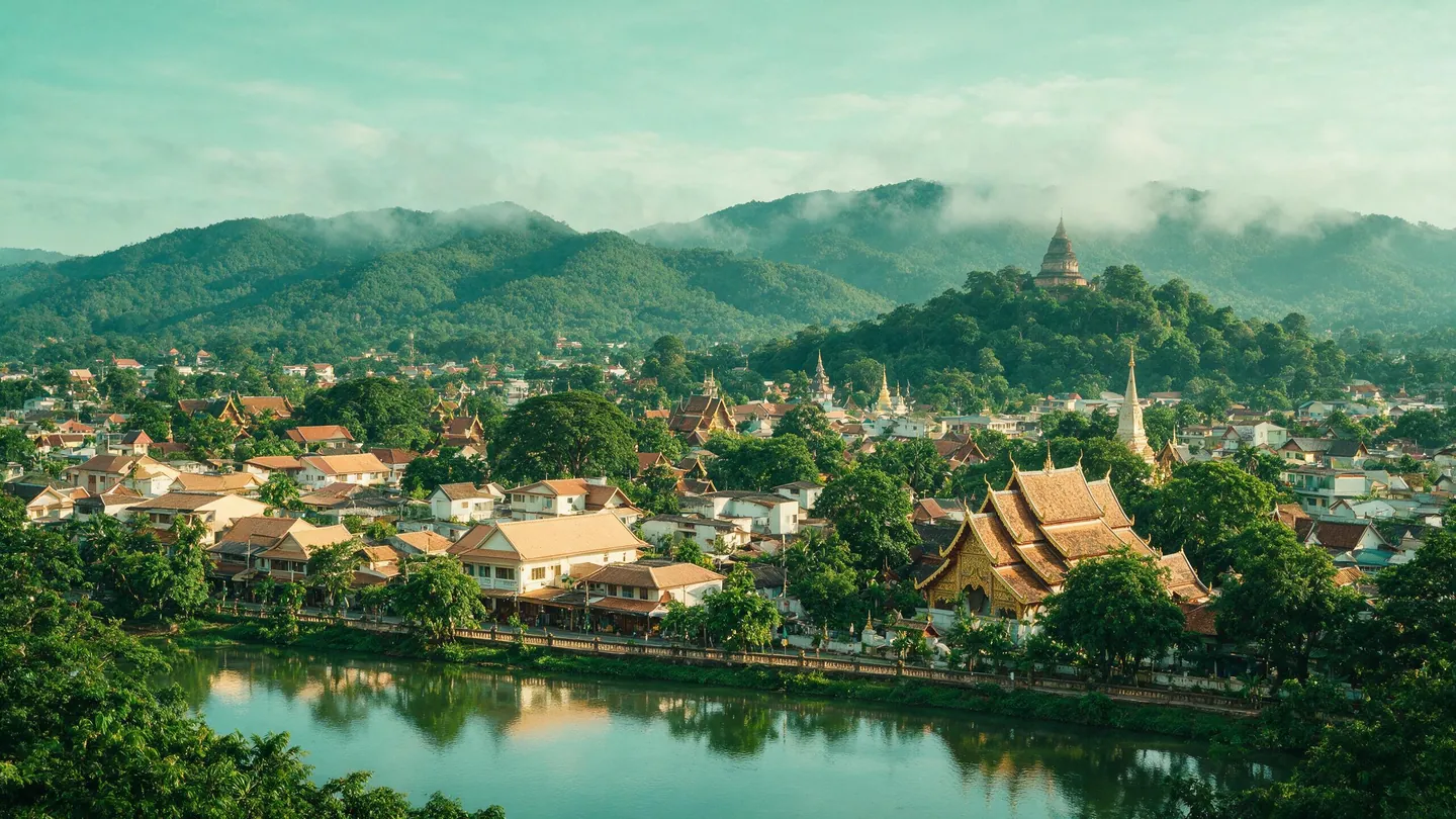เมืองเชียงใหม่ยามเช้า อาคารเตี้ย หลังคาวัดแบบล้านนา แม่น้ำ และแนวภูเขามีหมอกอยู่ด้านหลัง