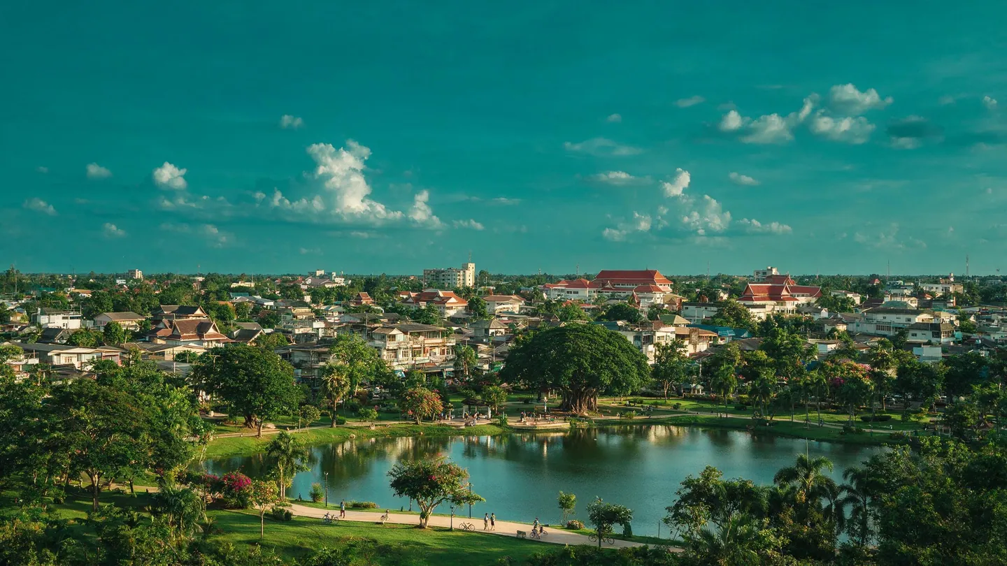 เมืองต่างจังหวัดมองจากมุมสูง มีบึงน้ำ สวนสาธารณะ และบ้านเรือนแนวราบ